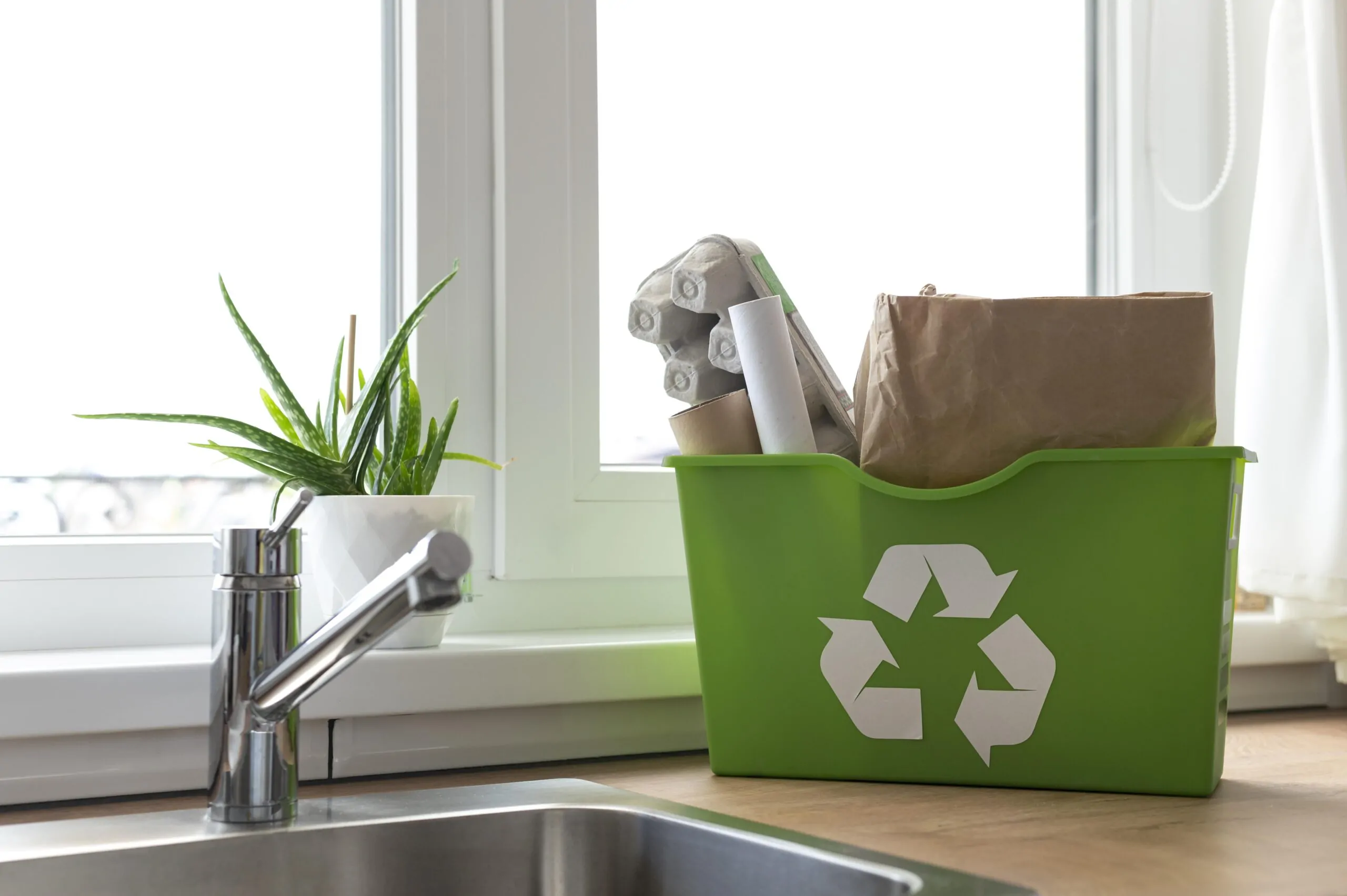 small recycle bin filled with recylced items placed near the sink in a kitchen